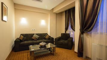 A modern living room with a dark green sofa, a glass coffee table, and a patterned rug.