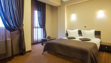 A hotel room with a large bed, a bedside table, a lamp, and a window with curtains.