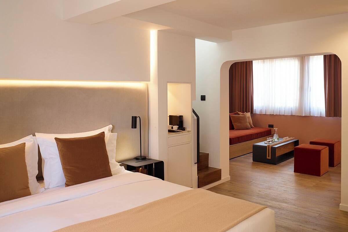 A modern hotel room with a large bed, a desk, a sofa, and a staircase leading to another room.