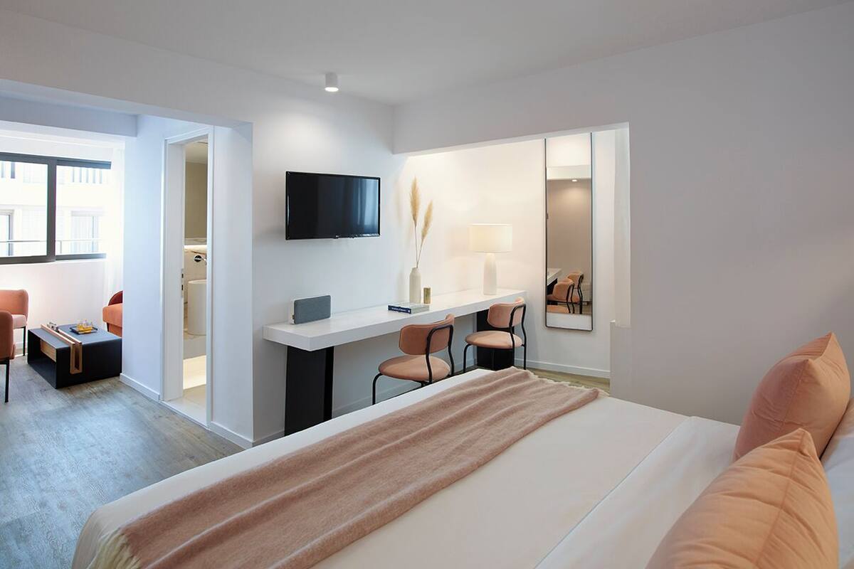A modern hotel room with a large bed, a desk with chairs, a TV, and a window.