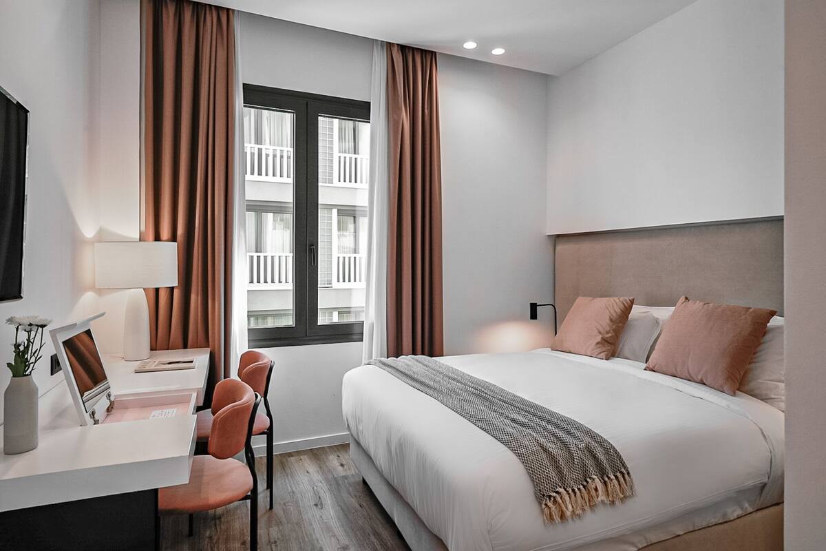 A modern hotel room with a bed, desk, and chairs.