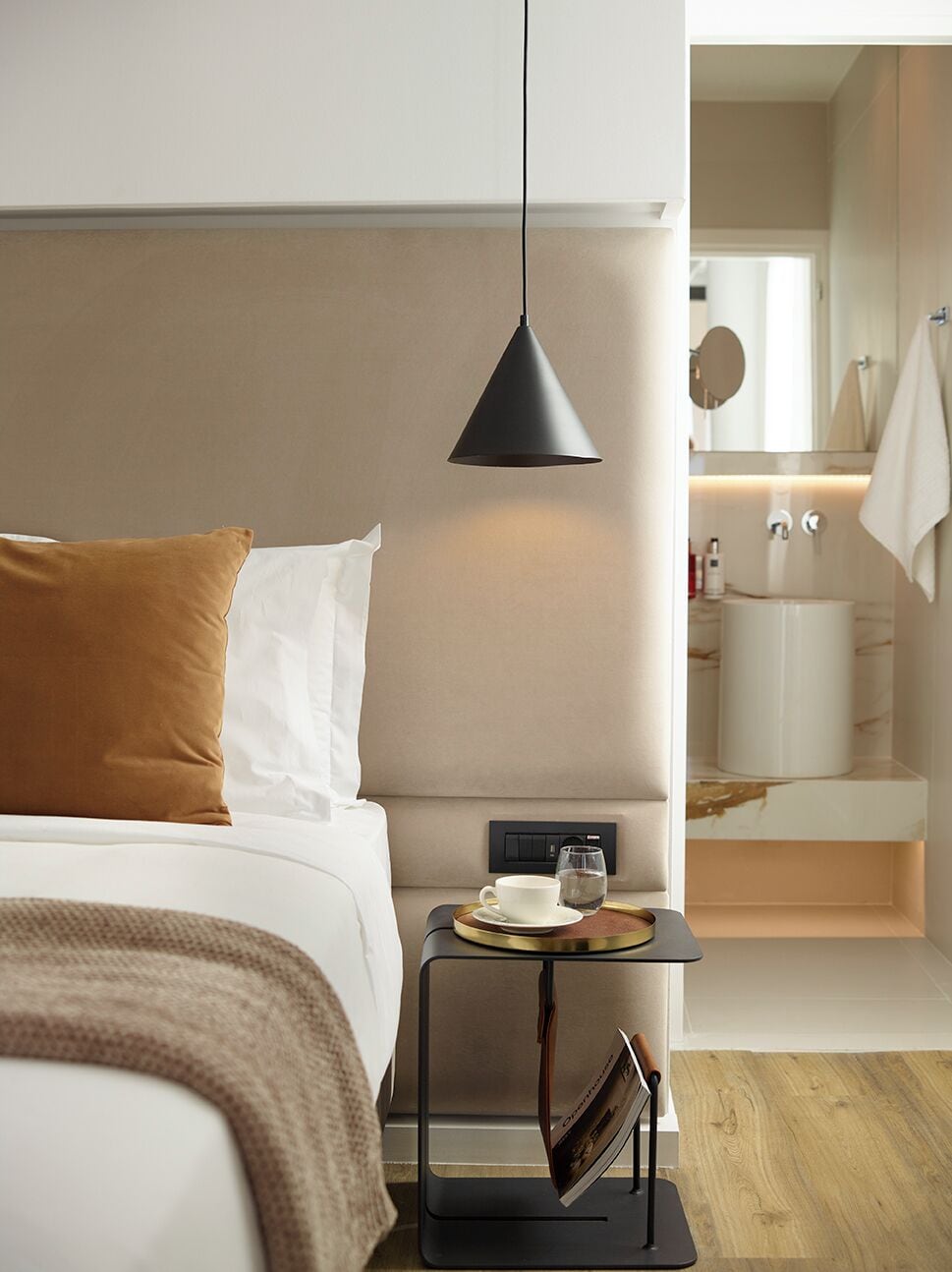 Una camera d'albergo moderna con un letto, un comodino, una lampada e vista sul bagno.