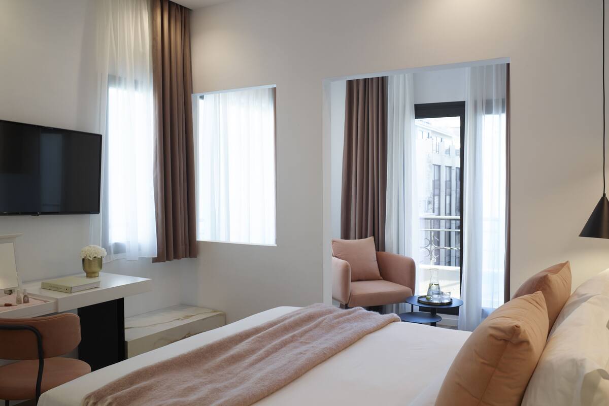 A hotel room with a bed, a desk, a chair, a TV, and large windows with curtains.