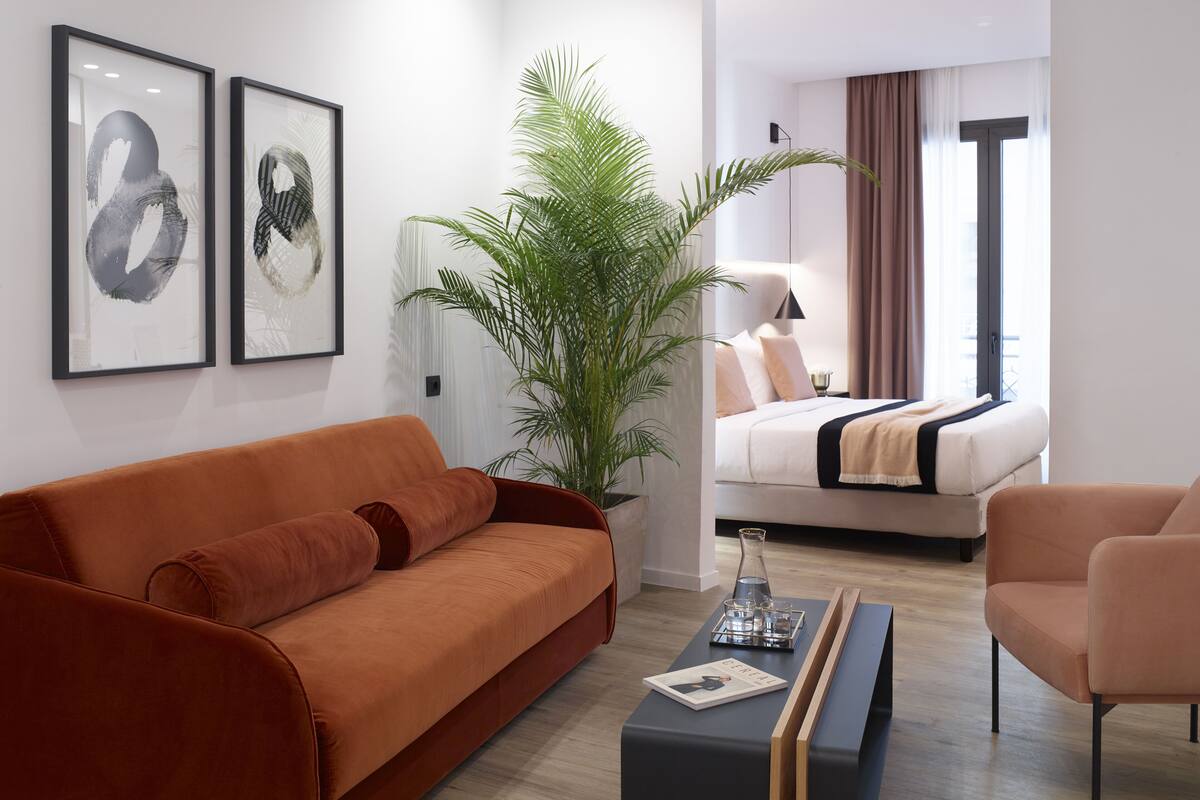 A modern hotel room with a sofa, a coffee table, a bed, and a large plant.