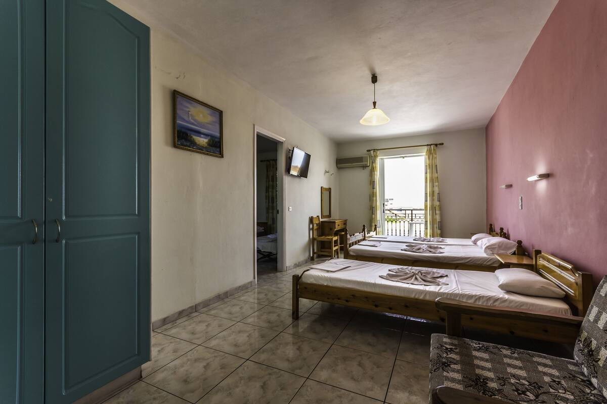 Une chambre avec deux lits en bois, un bureau, une chaise, une télévision et une armoire.