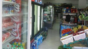 En butiksinredning med ett kylskåp för varuexponering, hyllor fyllda med olika produkter och en kassa.