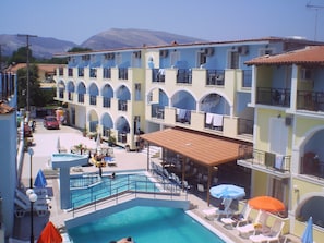 A hotel with a swimming pool, outdoor seating, and a view of mountains. - Vossos Hotel Apartments (Zakynthos)