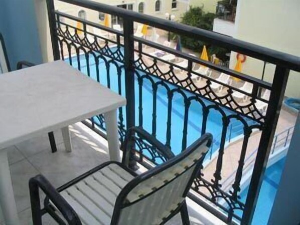 A balcony with a table and chair, overlooking a swimming pool and buildings. - Vossos Hotel Apartments (Zakynthos)