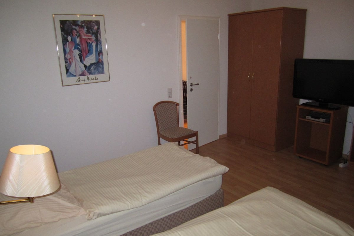 Ein Zimmer mit zwei Betten, einem Sessel, einem Fernseher und einem Kleiderschrank.