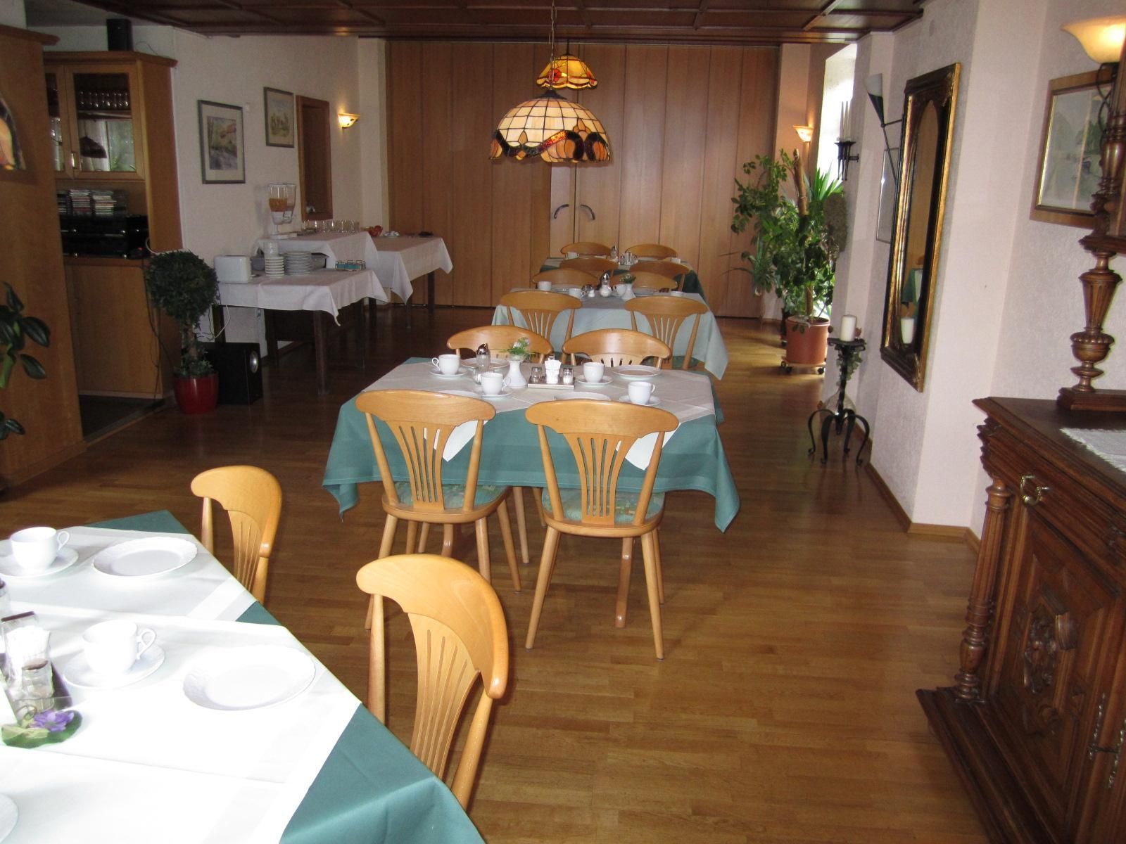 Un comedor con varias mesas dispuestas para recibir comensales, sillas de madera y una lámpara colgante.