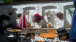 Een terras buiten met tafels, stoelen, potplanten en een rood-witte parasol.