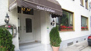Een hotelentree met een bruin luifel, een deur, een raam met rode bloemen, en twee potplanten.