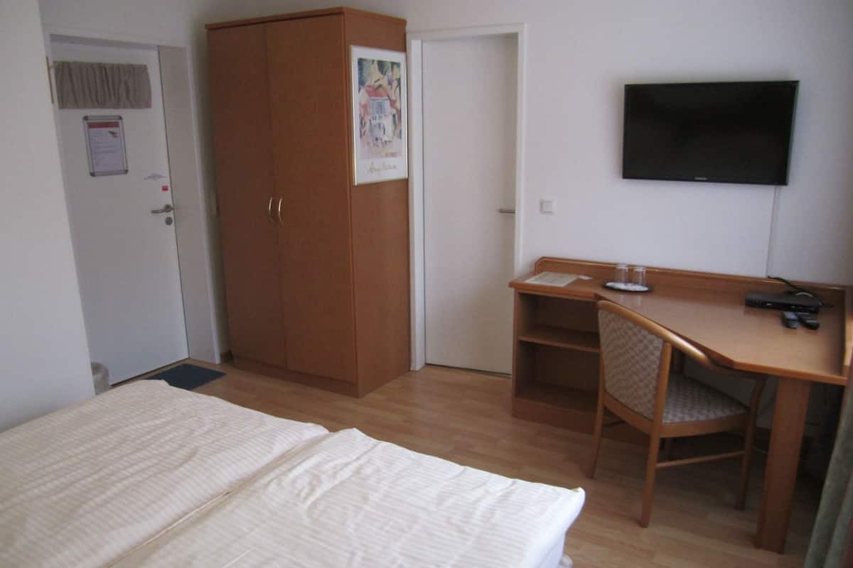 Ein Schlafzimmer mit einem Bett, einem Holzschrank, einem Schreibtisch mit Stuhl und einem an der Wand befestigten Flachbildfernseher.
