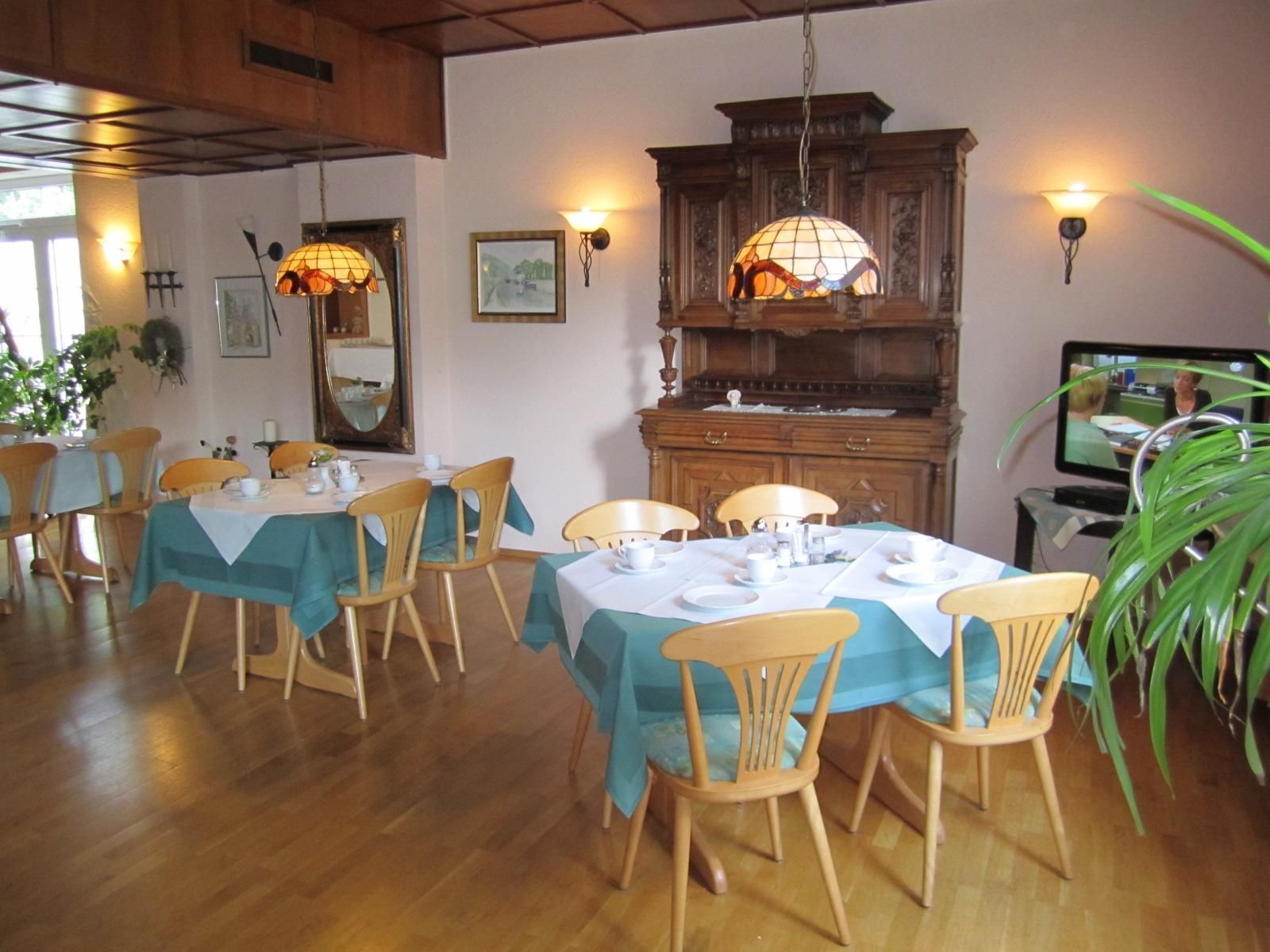 A dining area with wooden tables and chairs, a large wooden cabinet, and wall-mounted lamps.