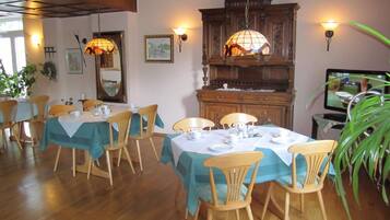 A dining area with wooden tables and chairs, a large wooden cabinet, and wall-mounted lamps.