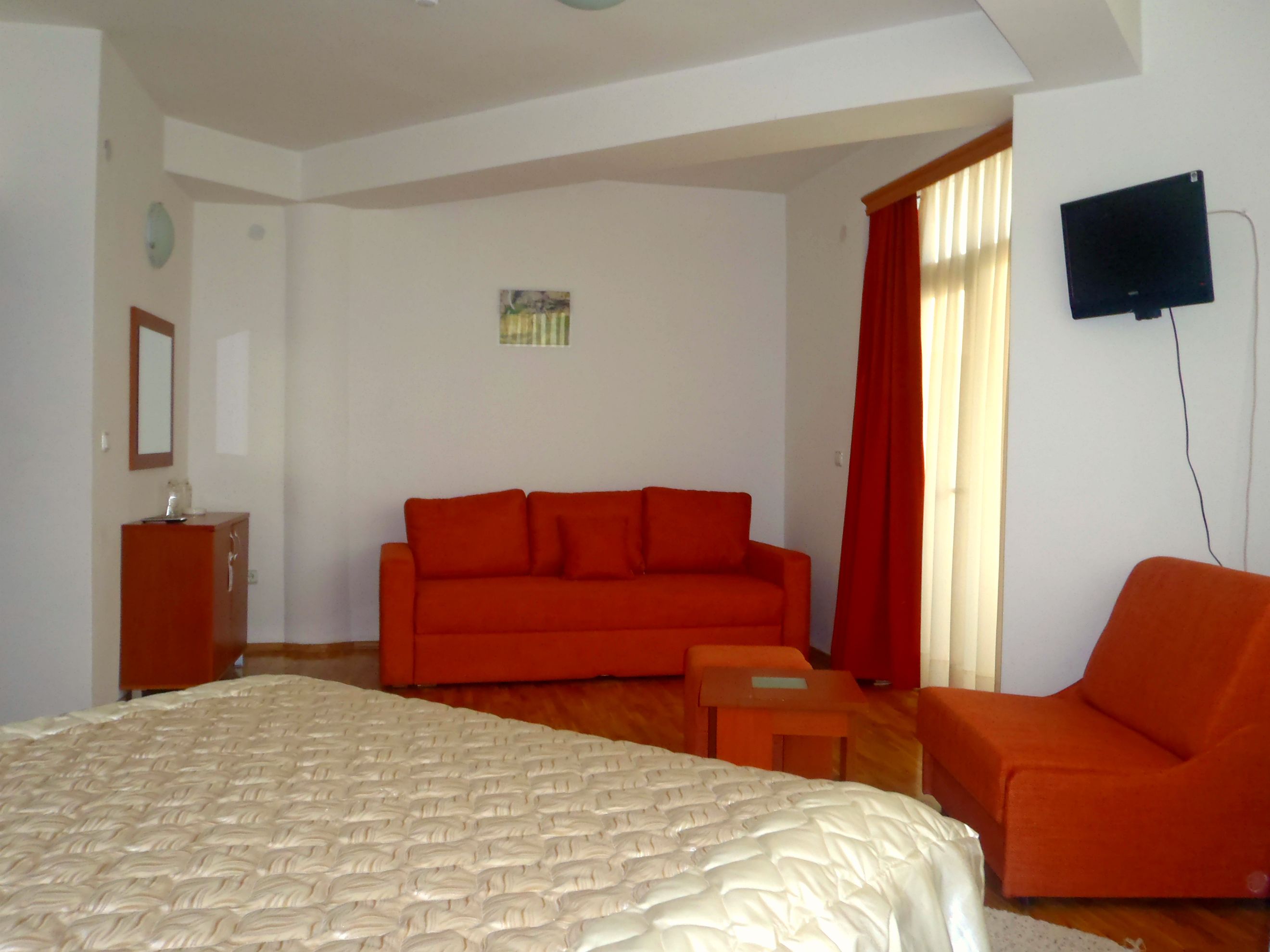 A hotel room with a large bed, a red sofa, a small table, and a TV mounted on the wall.