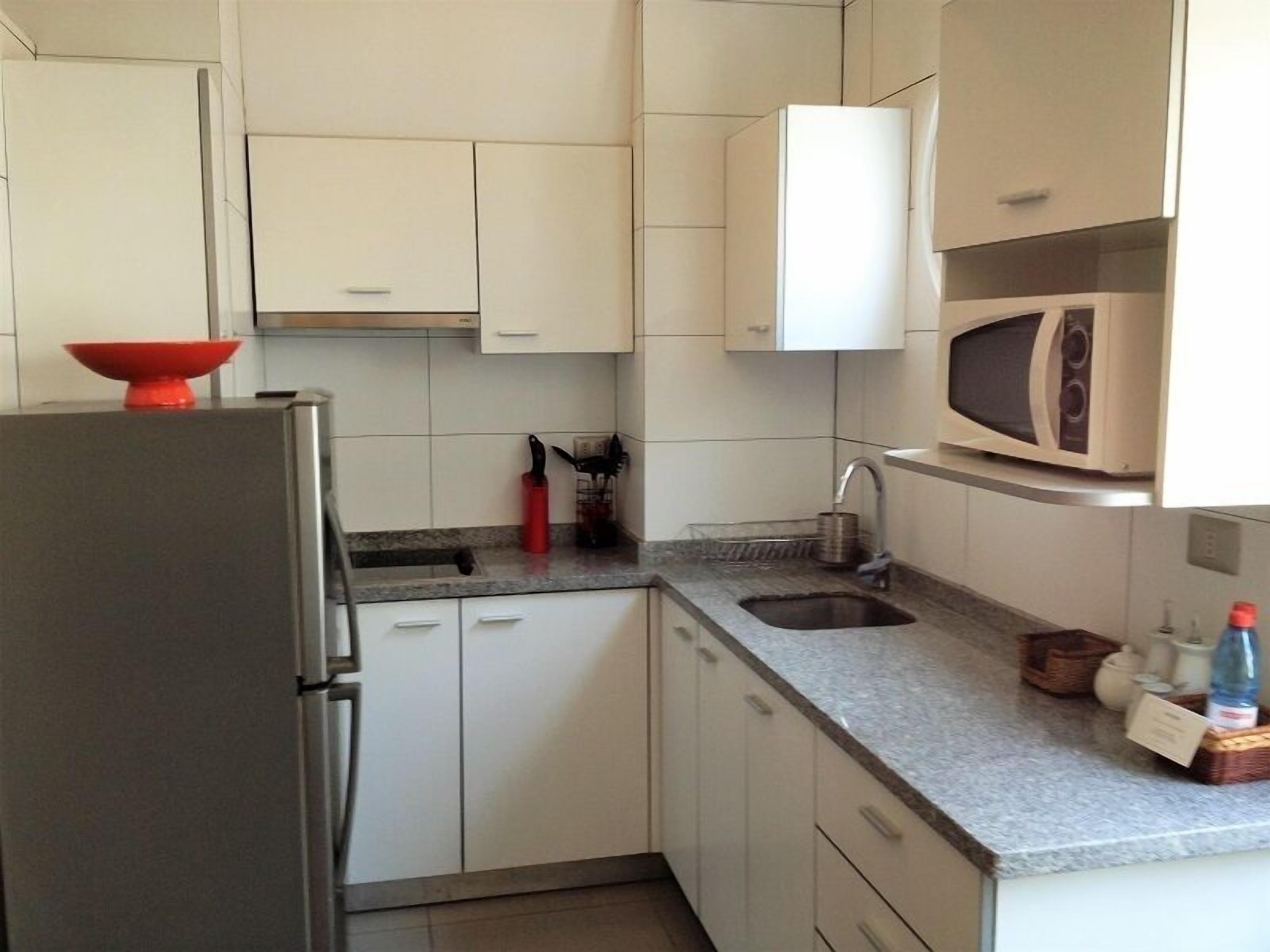 A compact kitchen with white cabinets, a stainless steel refrigerator, a microwave, and a sink.