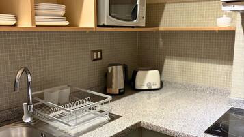 Uma cozinha equipada com micro-ondas, chaleira, torradeira e escorredor de pratos.