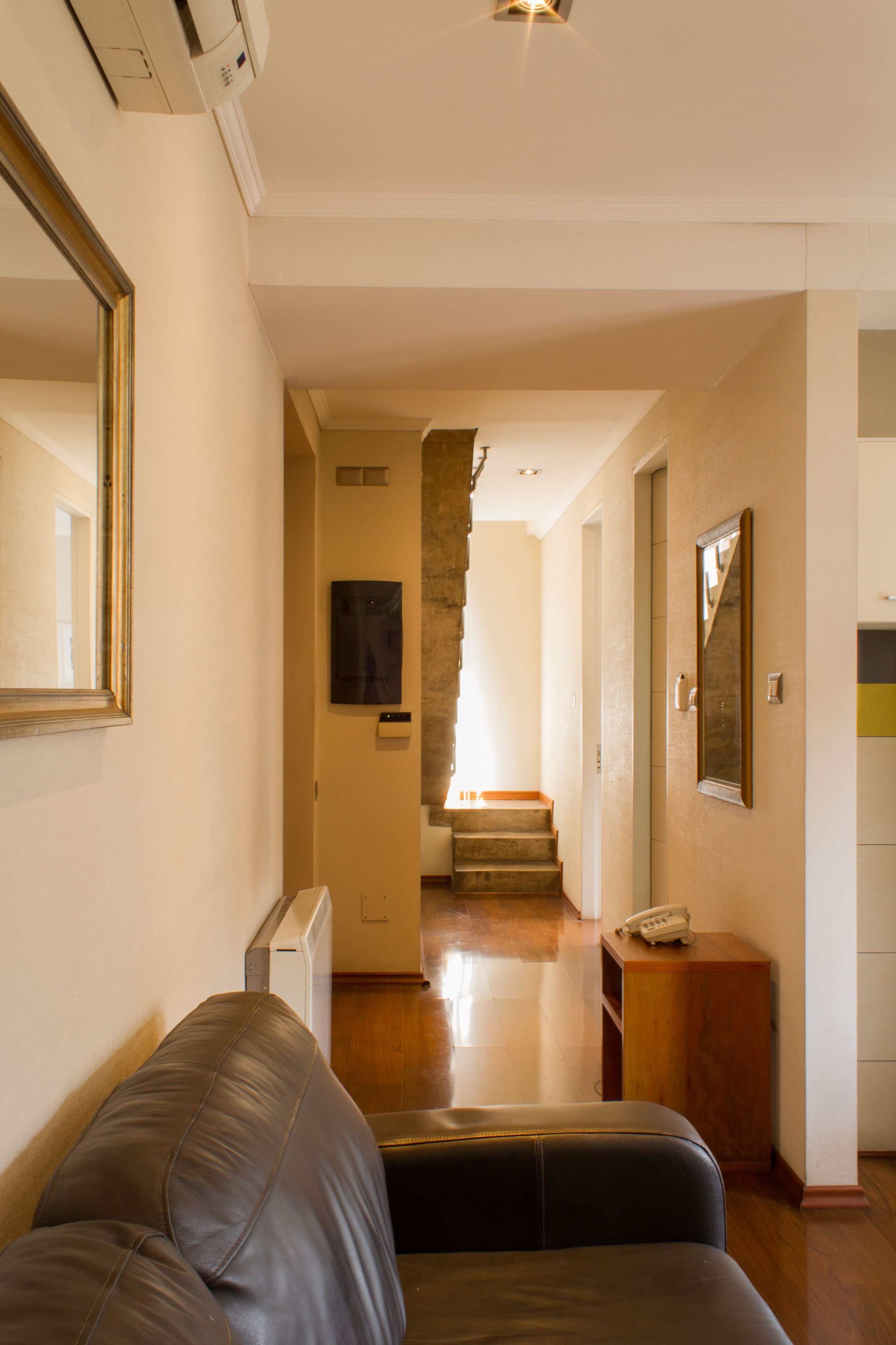 A hallway with a staircase, a leather sofa, a wooden cabinet, and a mirror on the wall.