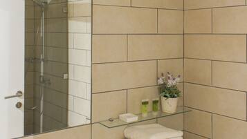 A bathroom with beige tiles, a glass shower enclosure, a sink, and a stack of towels.