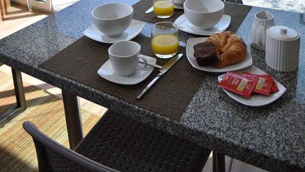 A breakfast table with a croissant, coffee cups, and juice, set on a balcony with a city view. - Lastarria Aparts (Santiago)