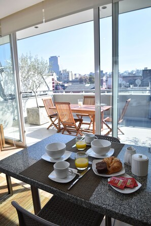 A breakfast table with a croissant, coffee cups, and juice, set on a balcony with a city view. - Lastarria Aparts (Santiago)