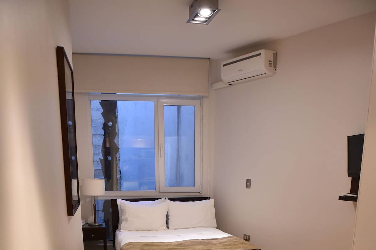 Una habitación de hotel con una cama, un escritorio con una computadora portátil, una silla y una ventana con cortinas.