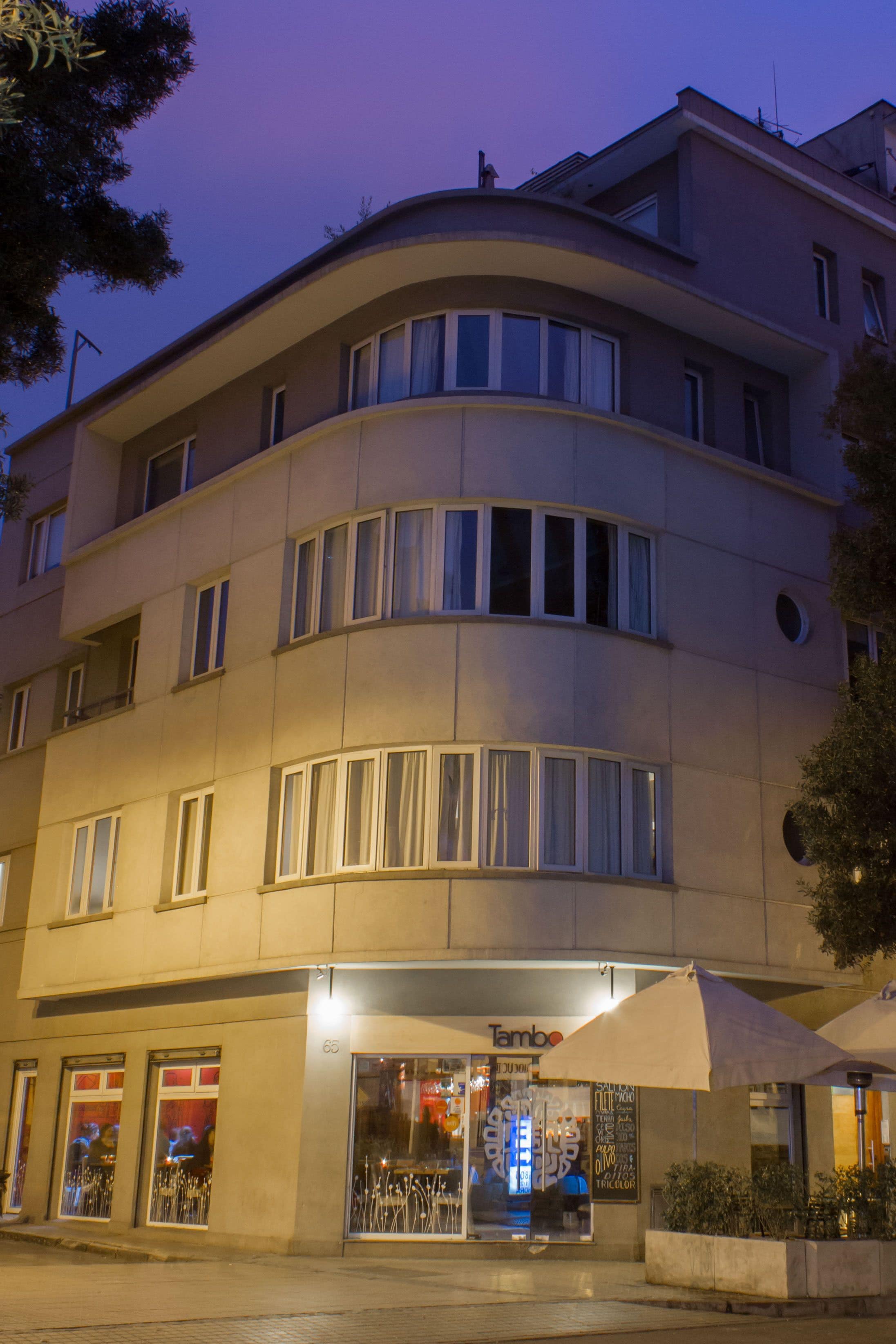 A multi-story building with a curved facade, large windows, and a ground-level storefront with an umbrella.