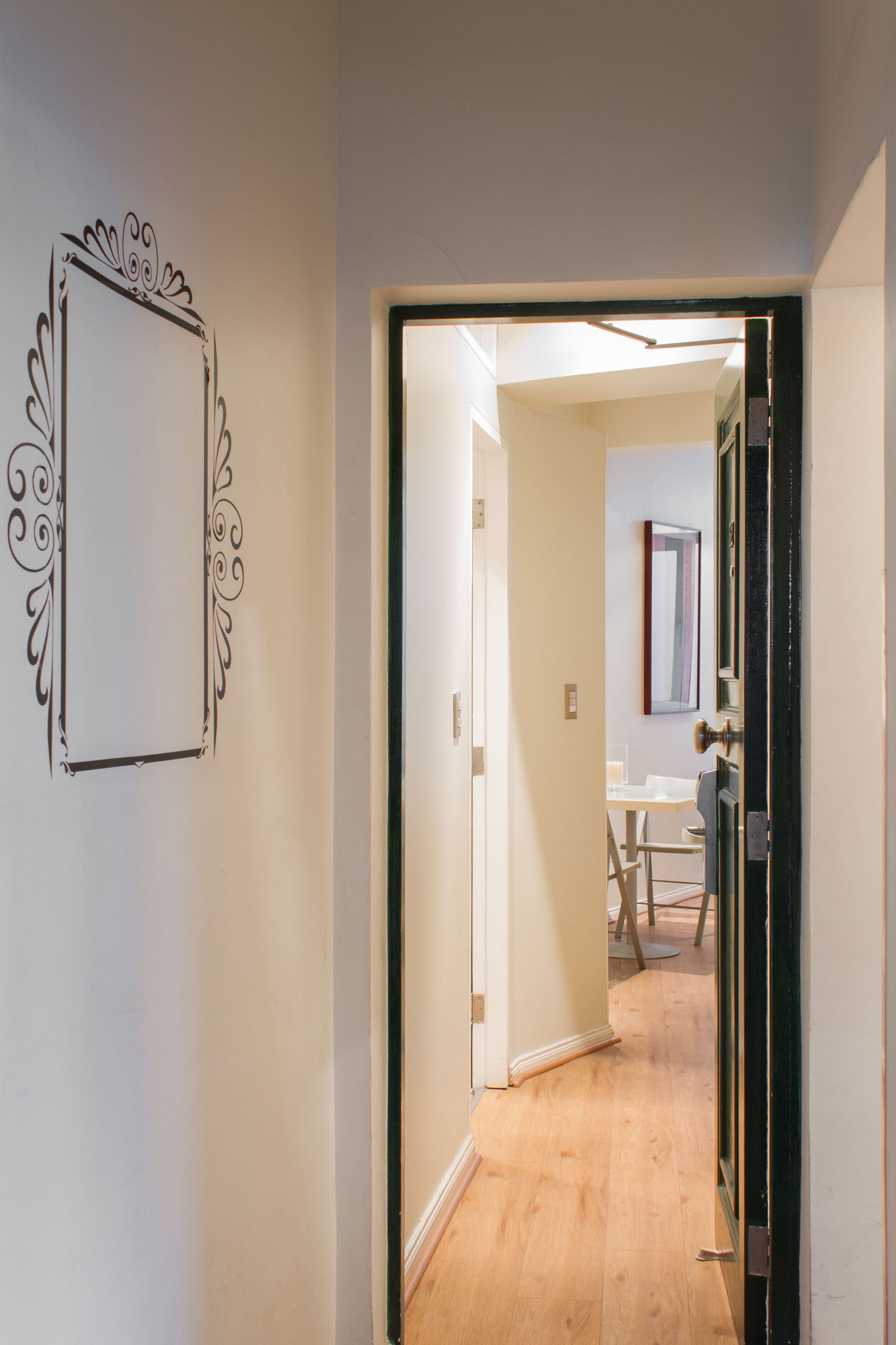 A hallway with a decorative wall frame, a wooden floor, and a door leading to a room with a table and chairs.