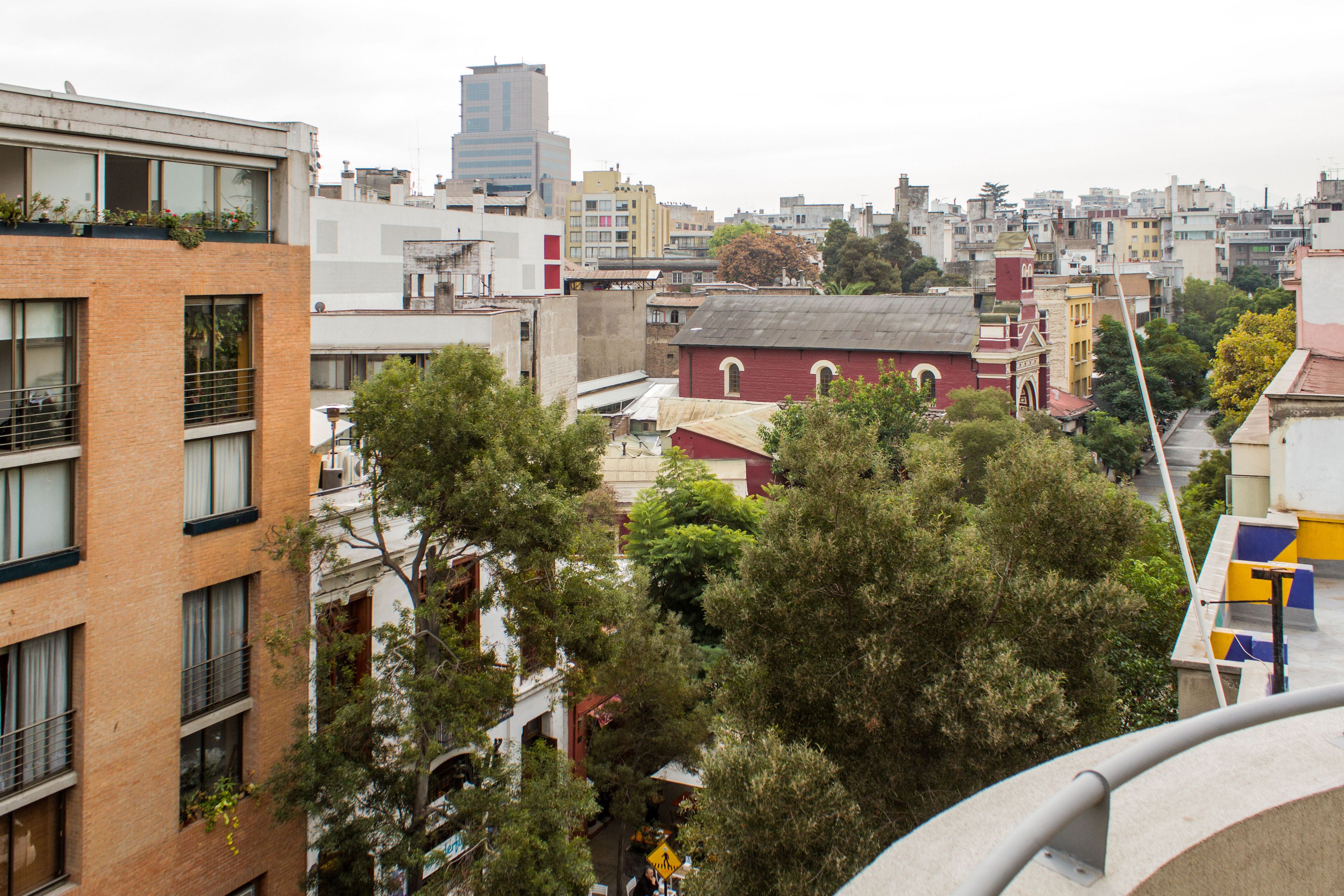Un paisaje urbano con diversos edificios, incluyendo una construcción de ladrillo rojo con múltiples ventanas y balcones, y un rascacielos moderno al fondo.