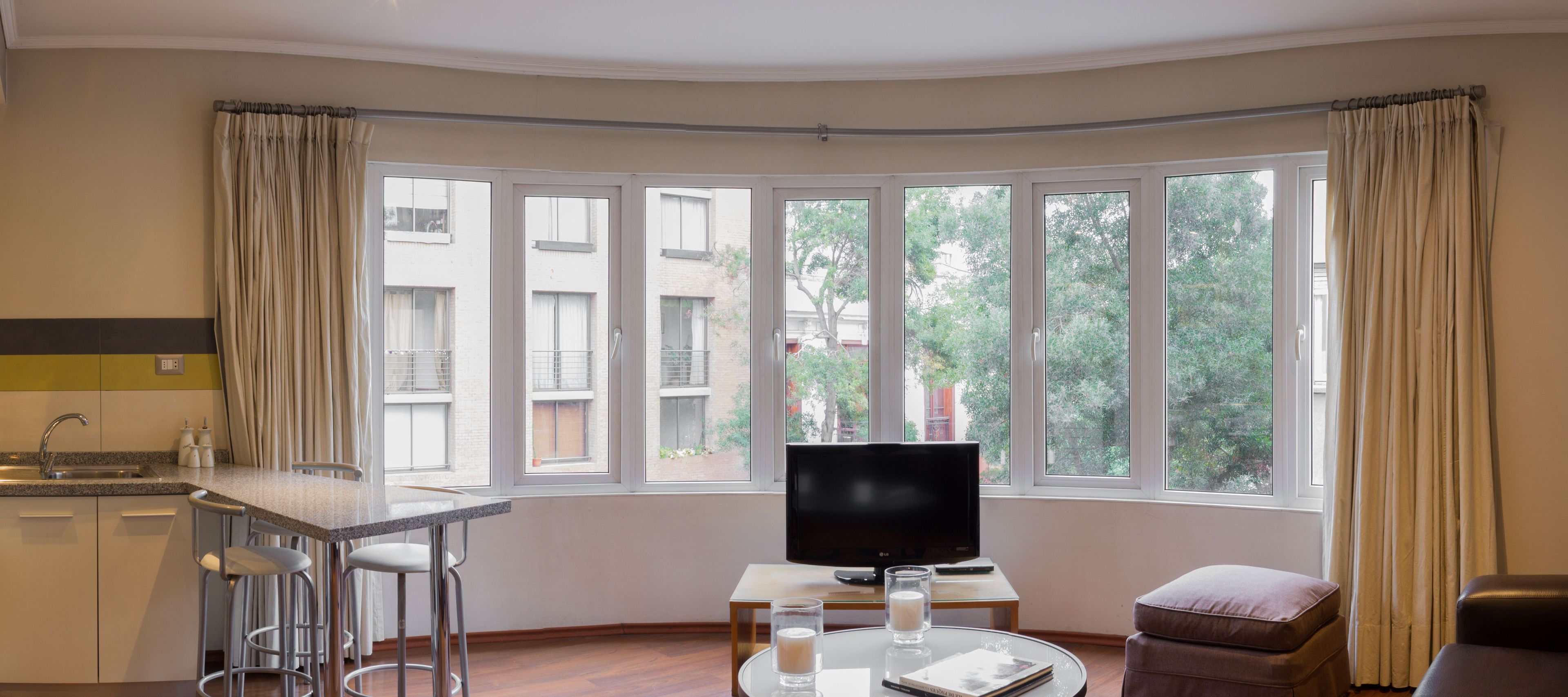 Una sala de estar moderna con un ventanal grande, un televisor de pantalla plana, una mesita con vasos y un libro, y un sofá.