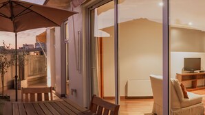A modern living room with a wooden table, a bench, and a sofa. There is a sliding glass door leading to a balcony with a view of the city. - Lastarria Aparts (Santiago)
