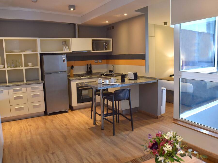 Eine moderne Küche mit integriertem Mikrowellenherd, Kaffeemaschine und Toaster. Ein Holztisch mit zwei Stühlen steht bereit.