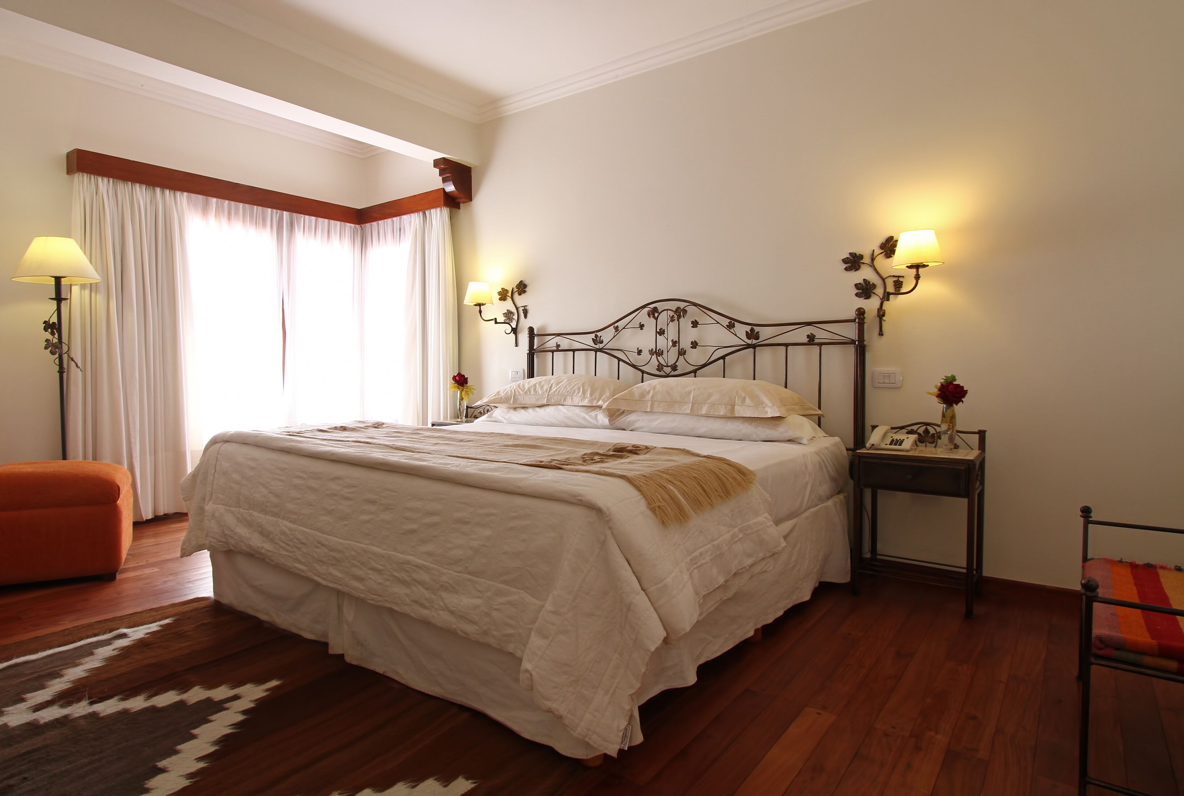 A neatly arranged bedroom with a large bed, two bedside tables with lamps, a chair, and a window with curtains.