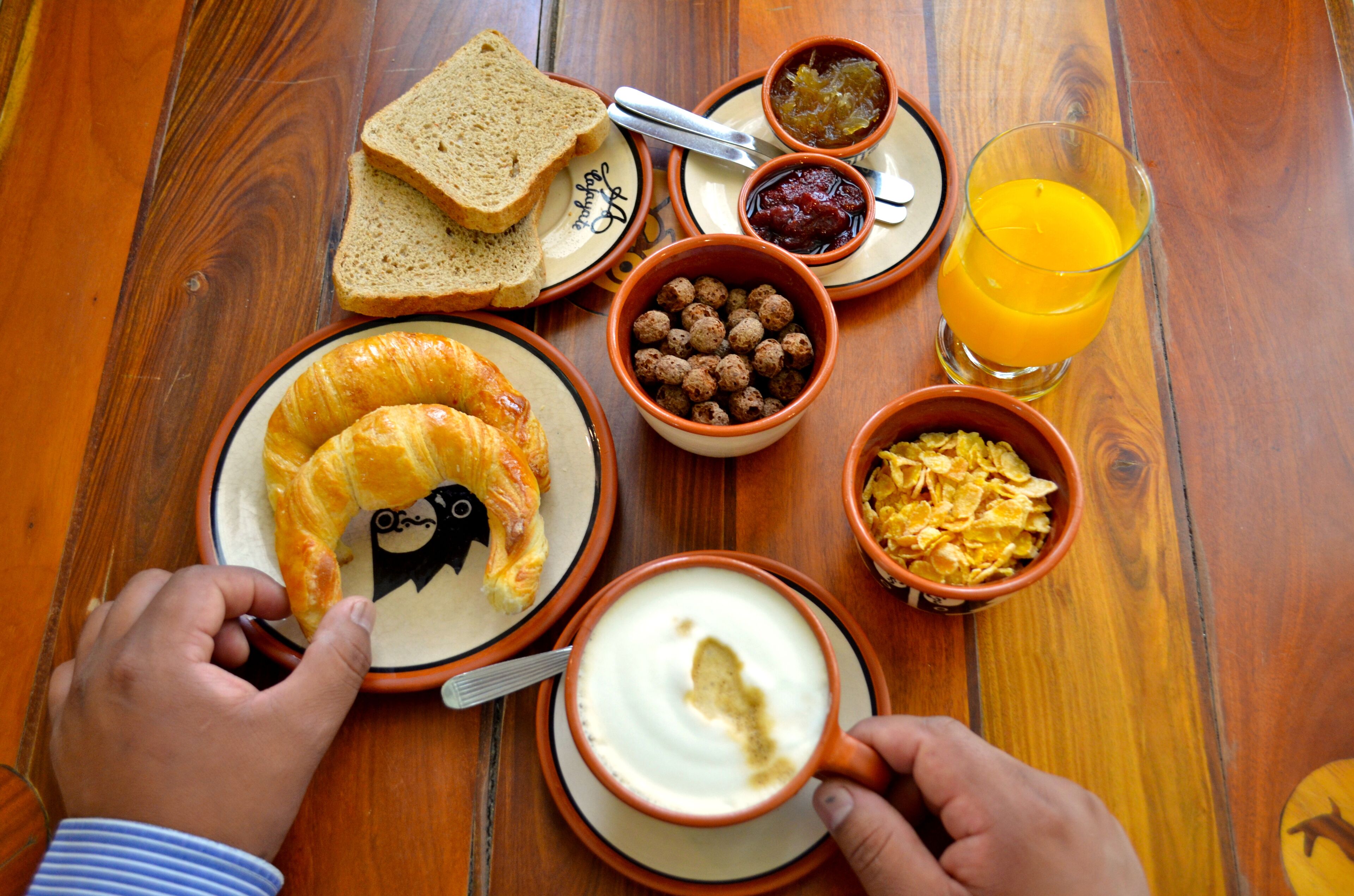 A wooden table with breakfast items including croissants, cereal, toast, jam, and orange juice.