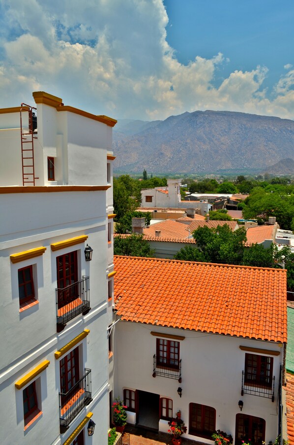 Un edificio blanco con tejados anaranjados y balcones, rodeado de vegetación y montañas al fondo.