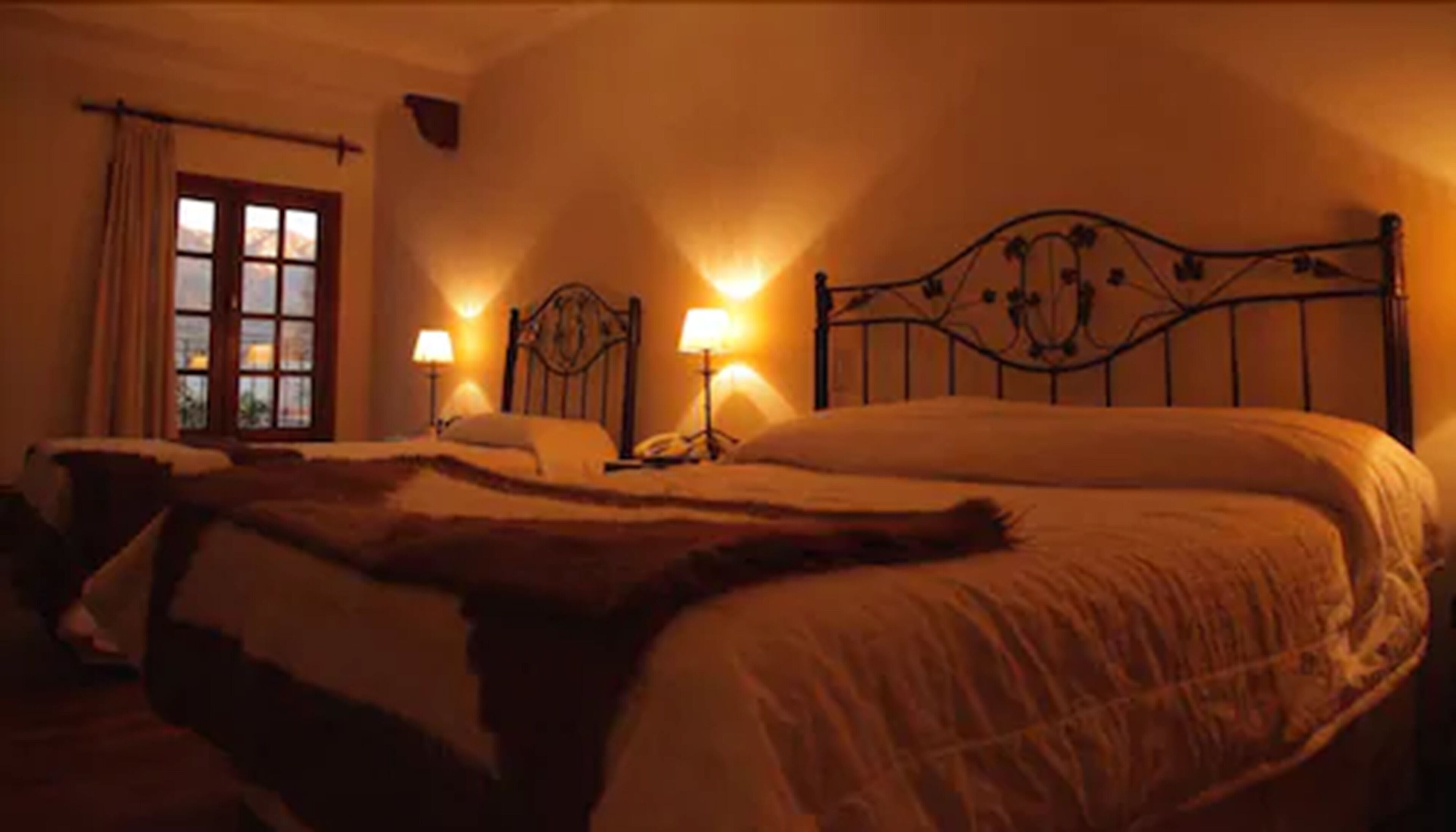 Un dormitorio tenuemente iluminado con una cama grande, dos lámparas de noche y una ventana con cortinas.