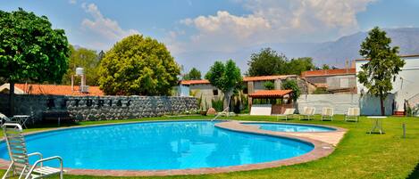 A swimming pool with a stone wall and a grassy area with chairs.