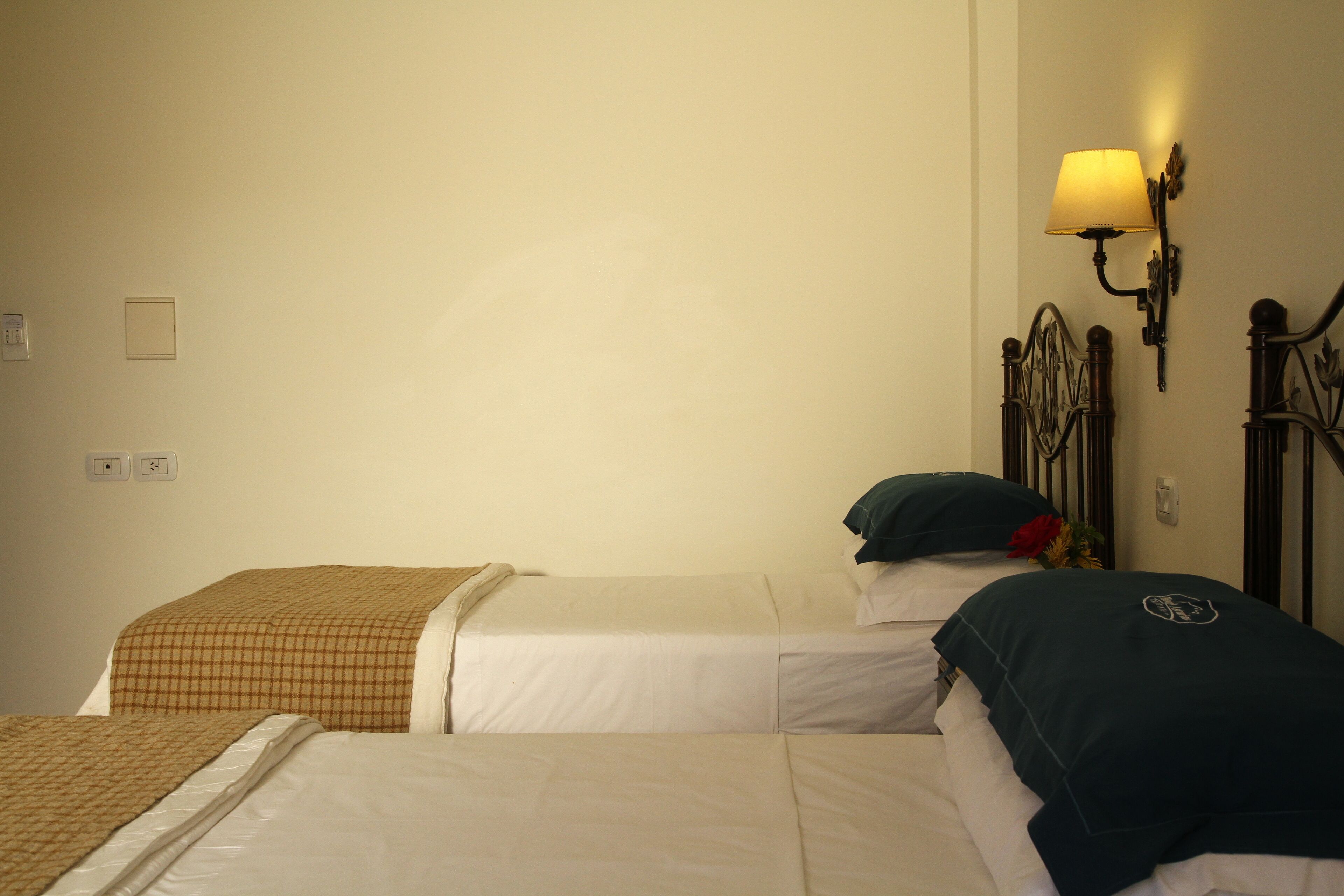 A hotel room with two single beds, a wall-mounted lamp, and a bed with a decorative pillow.