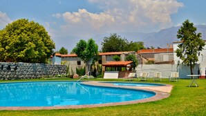 Una piscina con muro de piedra, sillas de descanso y vistas a las montañas.