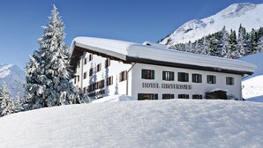 Un bâtiment enneigé portant l’enseigne « HÔTEL HINTERWIES », indiquant la présence d’un hôtel dans une région montagneuse couverte de neige.