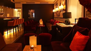 Un coin bar à la lumière tamisée, avec des chaises à revêtement rouge et un espace salon comprenant une table et une lampe.
