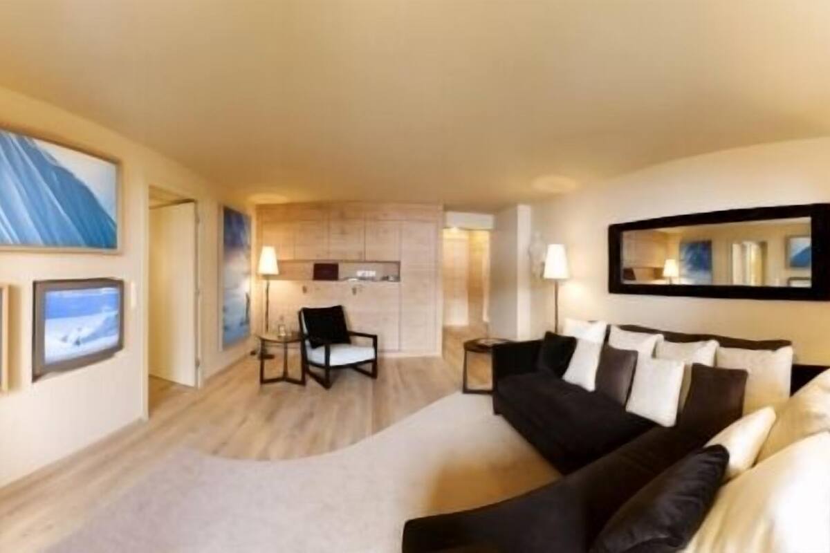 Hotellihuoneessa on musta sohva, pieni pöytä ja tuoli. Seinillä on kehystettyjä tauluja ja sohvan yläpuolella peili.