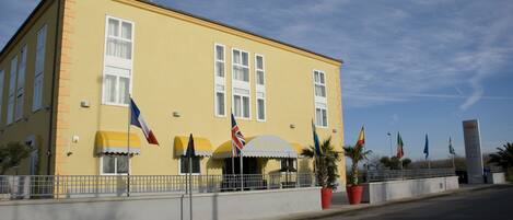 Un bâtiment jaune avec une enseigne indiquant « HÔTEL » et plusieurs drapeaux devant.