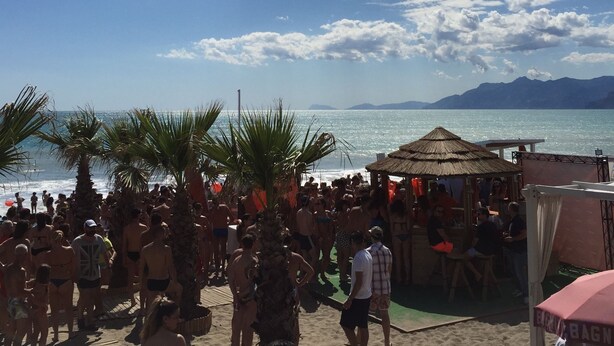 A crowded beach with palm trees and a thatched-roof structure. - La Isla Resort (Pontecagnano Faiano)