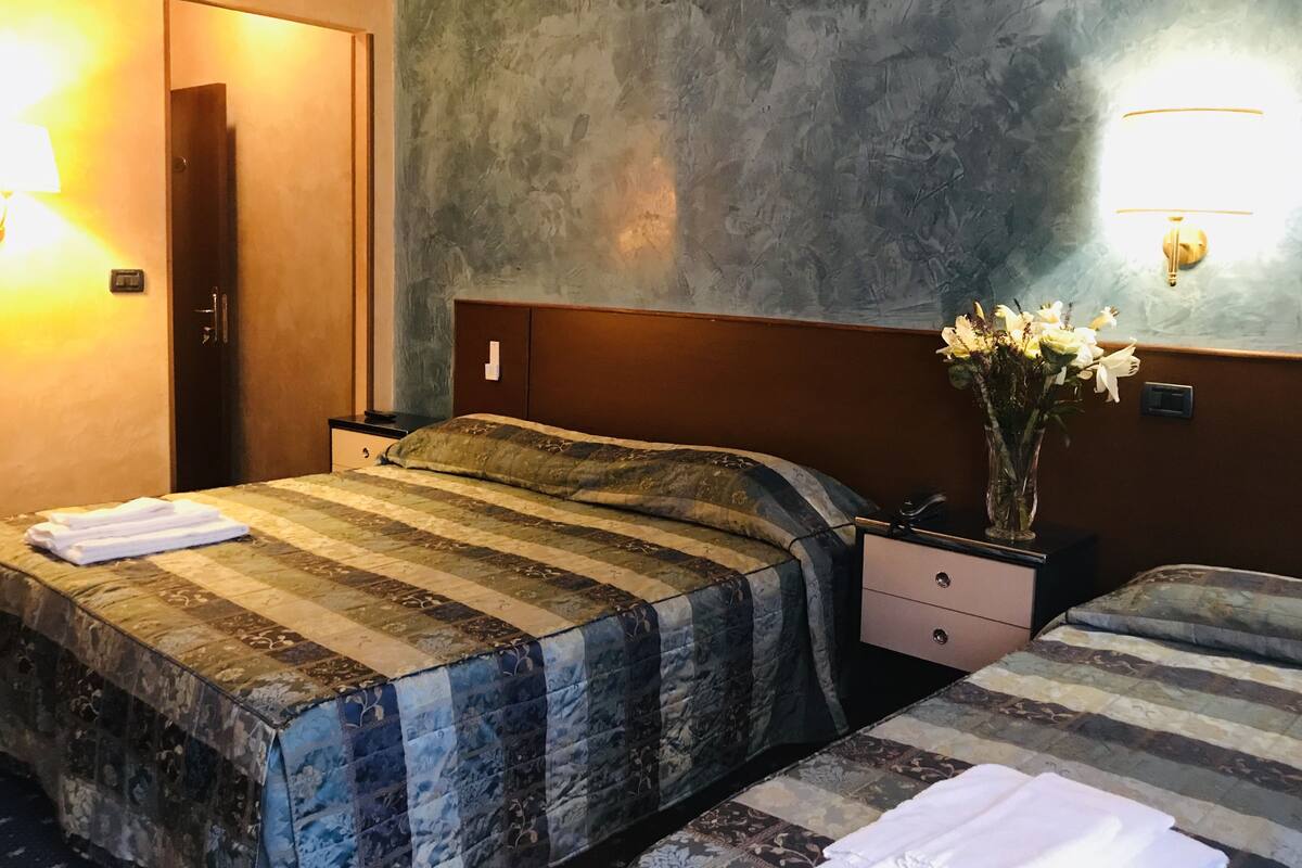 A hotel room with two beds, a nightstand, a vase with flowers, and a textured wall.