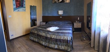 Una camera d'albergo con un letto grande, un comodino, una lampada, uno specchio e una tenda.