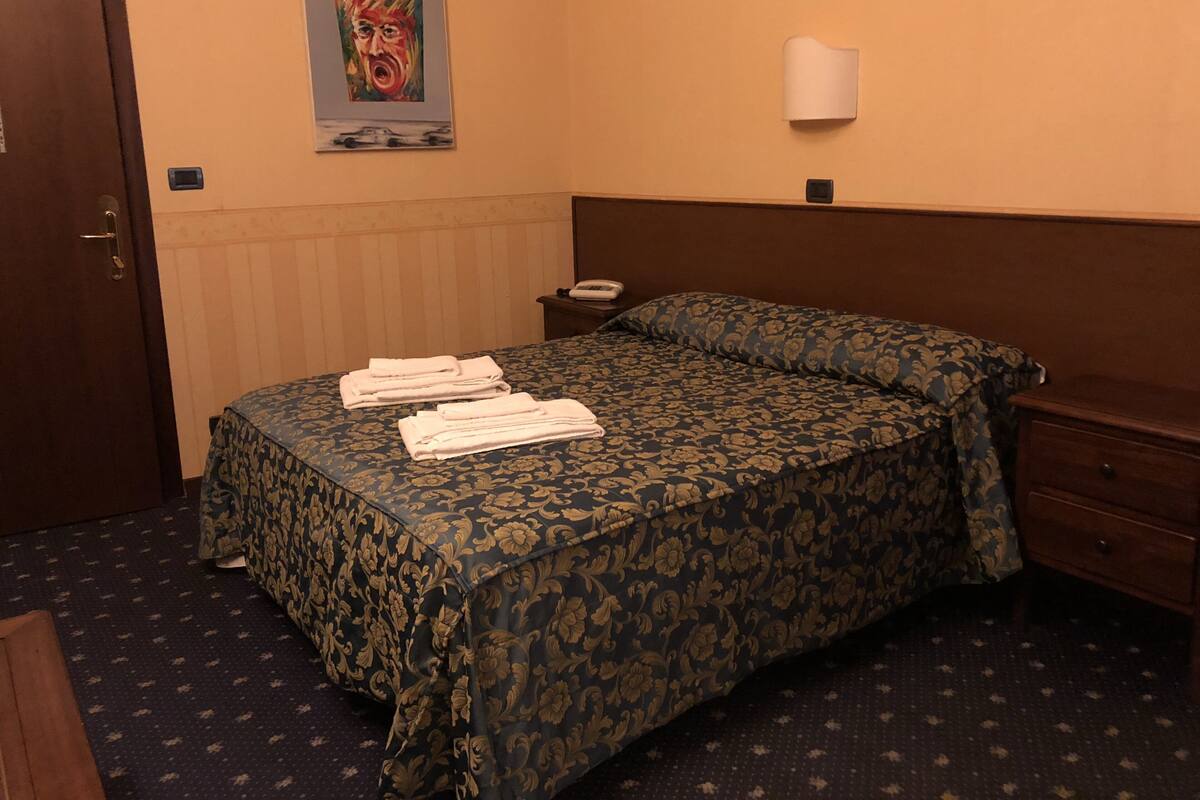 A hotel room with a bed, a nightstand, a telephone, and a poster on the wall.