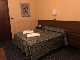 Una camera d'albergo con un letto, un comodino, un telefono e un quadro appeso al muro.