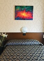 Una camera d'albergo con una coperta a motivi, un elemento decorativo a parete e un vaso con fiori.